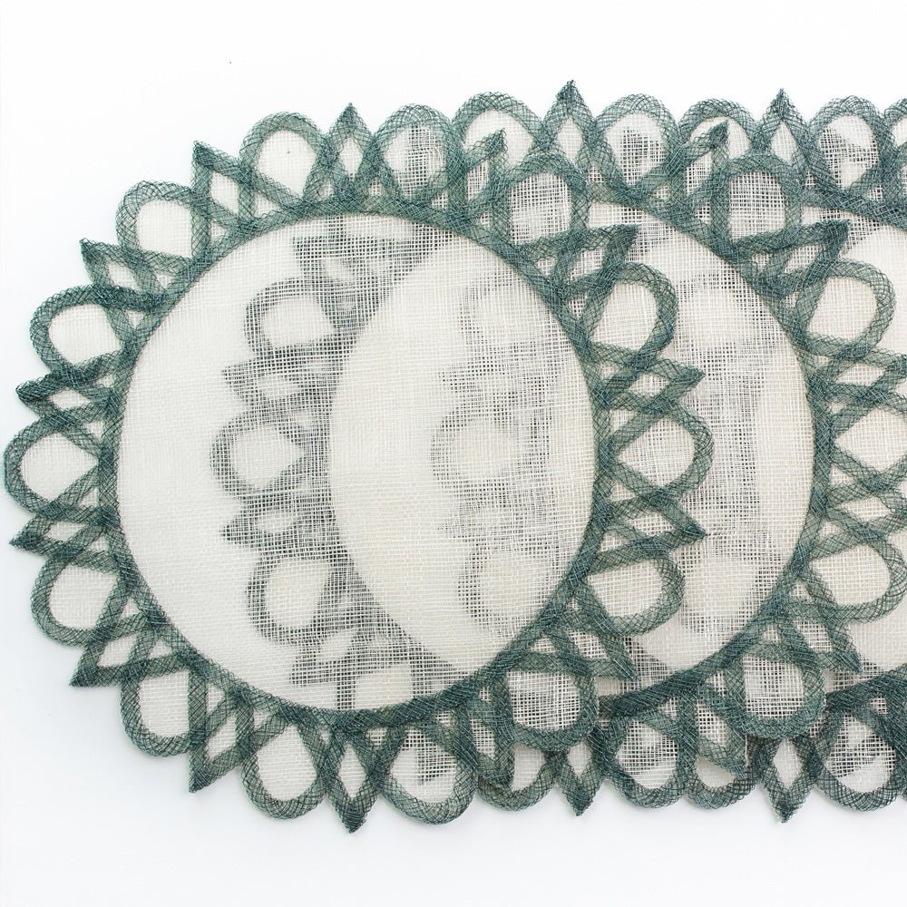 A set of round placemats with a central sun motif, predominantly white with green fretwork borders.