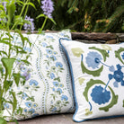 Two decorative pillows with floral patterns on a stone surface with greenery in the background.