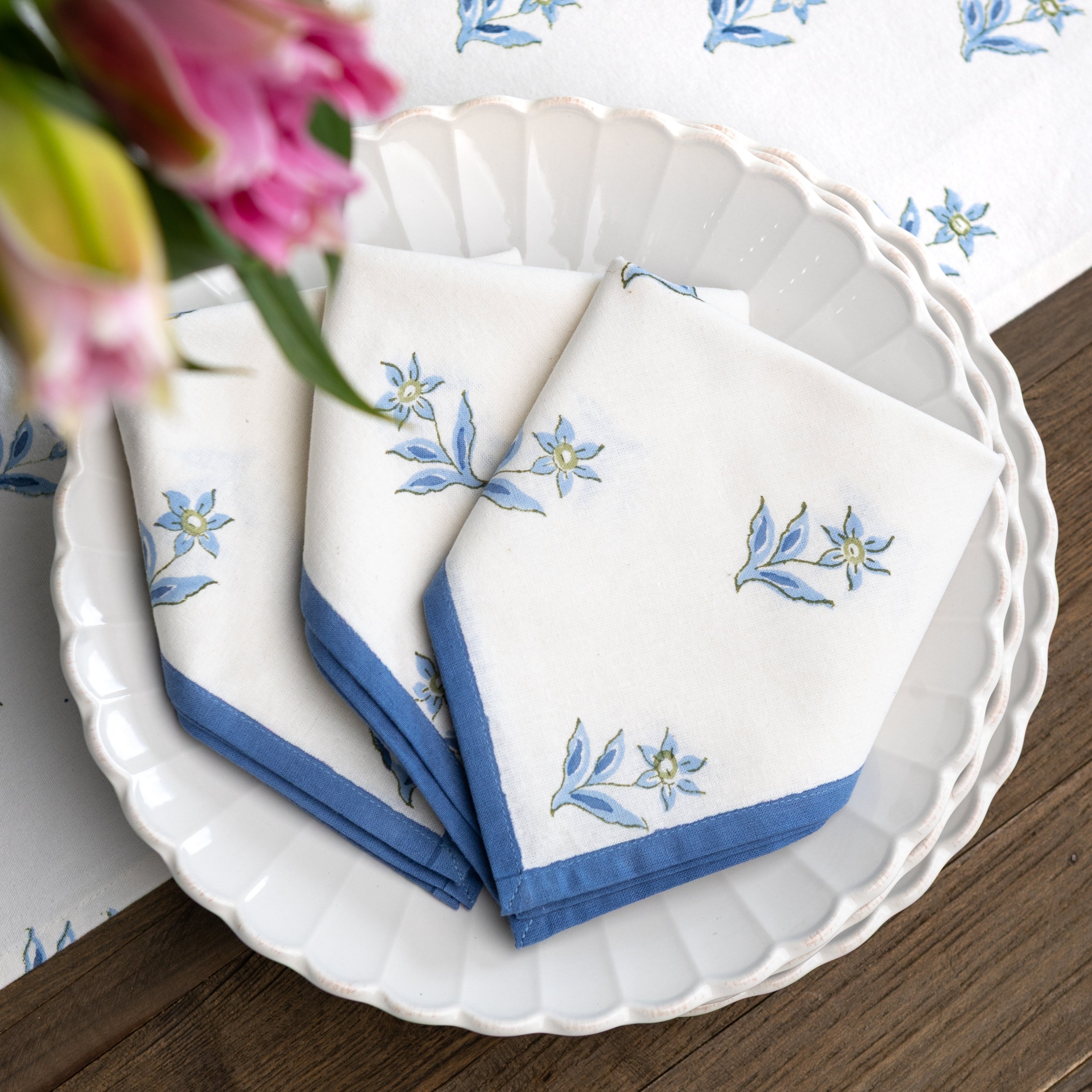White napkins with blue floral embroidery on a white plate with a floral-patterned tablecloth.