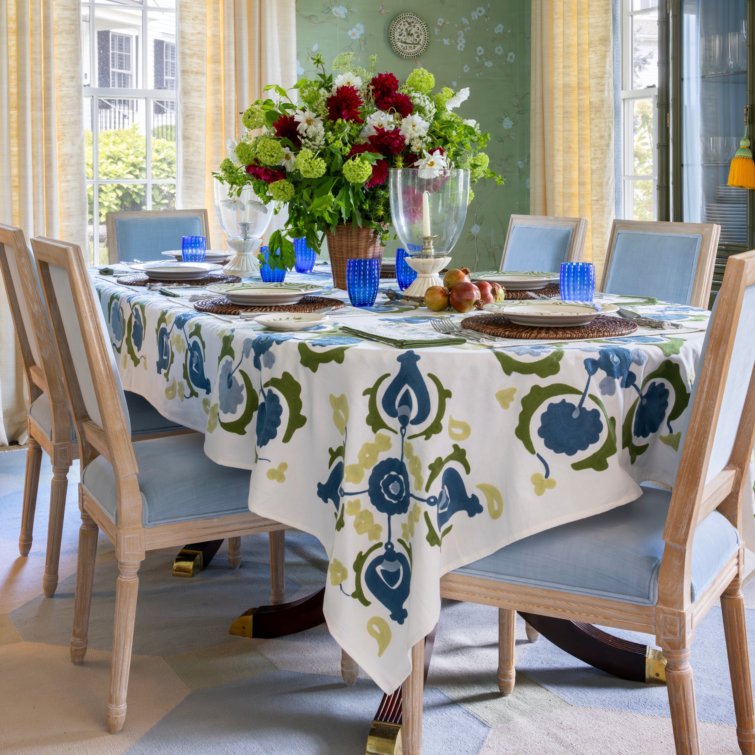 Dining room with a table set for a meal, featuring a floral centerpiece and patterned tablecloth.