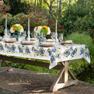 Dining table set with floral tablecloth, plates, glasses, and candles outdoors.