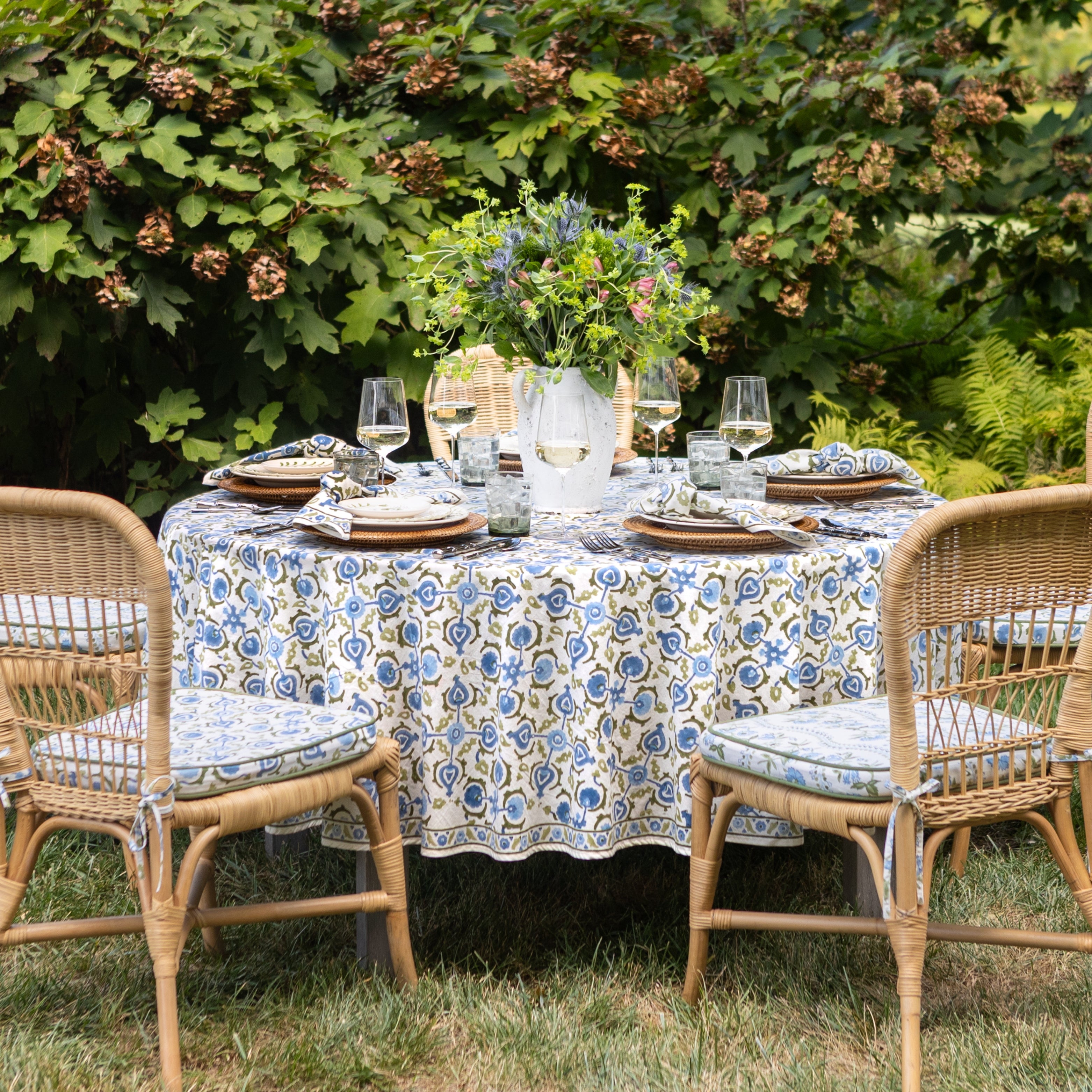 Outdoor dining setup with a patterned tablecloth, chairs, and floral centerpiece.