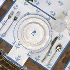 Set table with white plates, silverware, and a decorative blue floral placemat on a wooden table.
