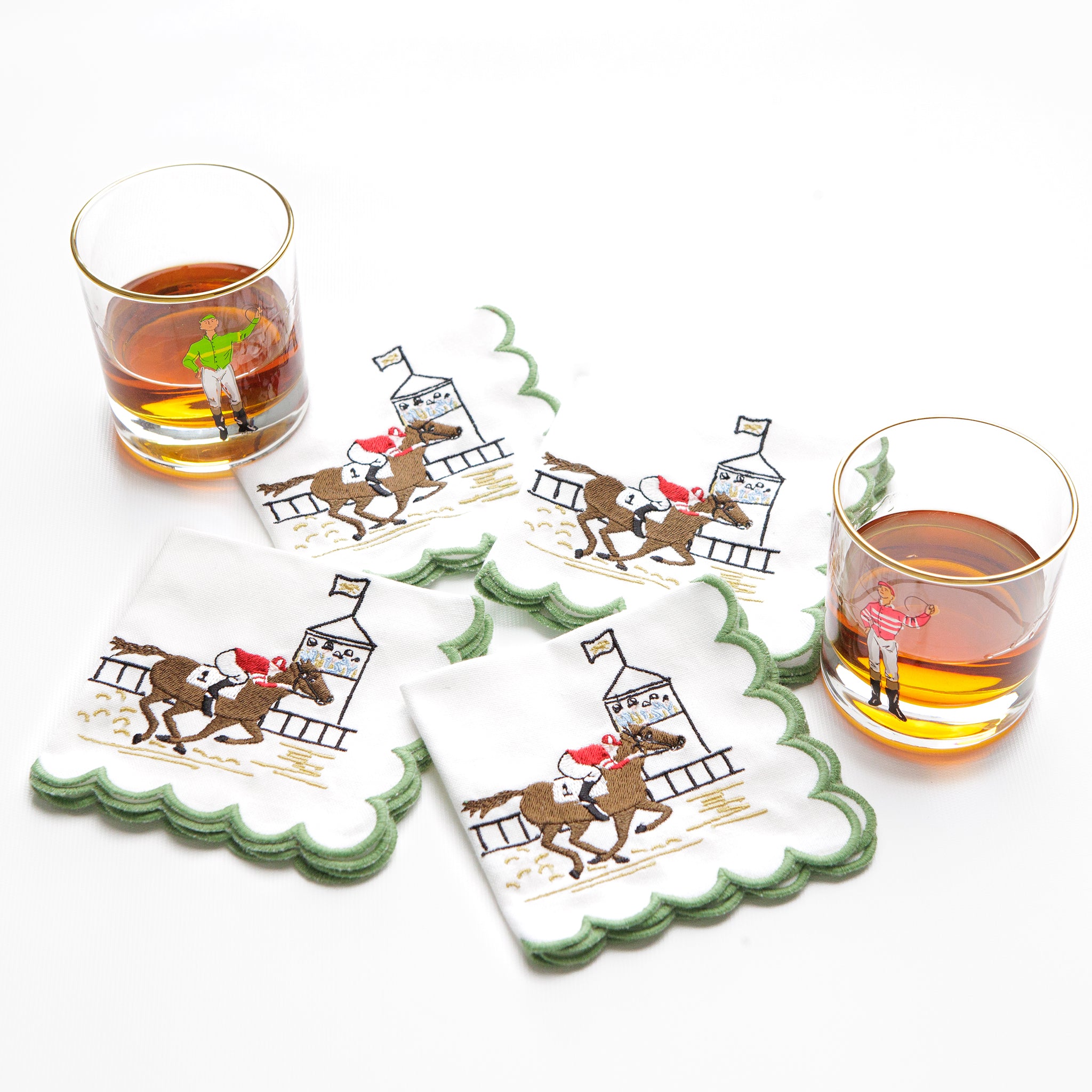 Set of four cocktail napkins with horse racing scene along with bourbon glasses on a white background