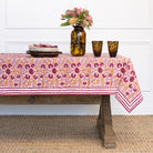 Table with a patterned tablecloth, flowers, and glasses against a white wall.