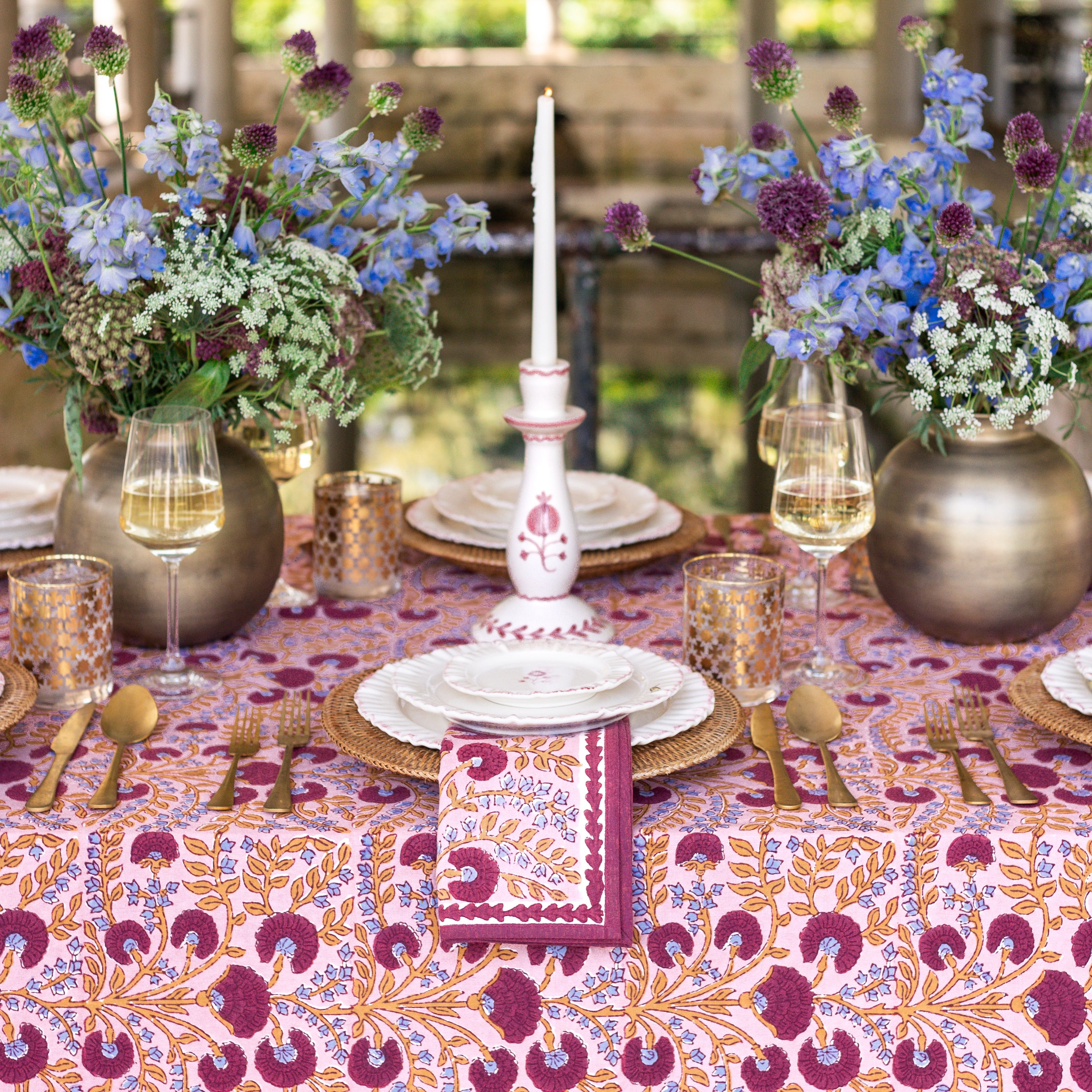 Elegant table setting with floral centerpieces, candles, and patterned tablecloth.