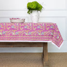 A dining table with the Climbing Dahlia Lilac Tablecloth featuring a floral design, placed against a white background