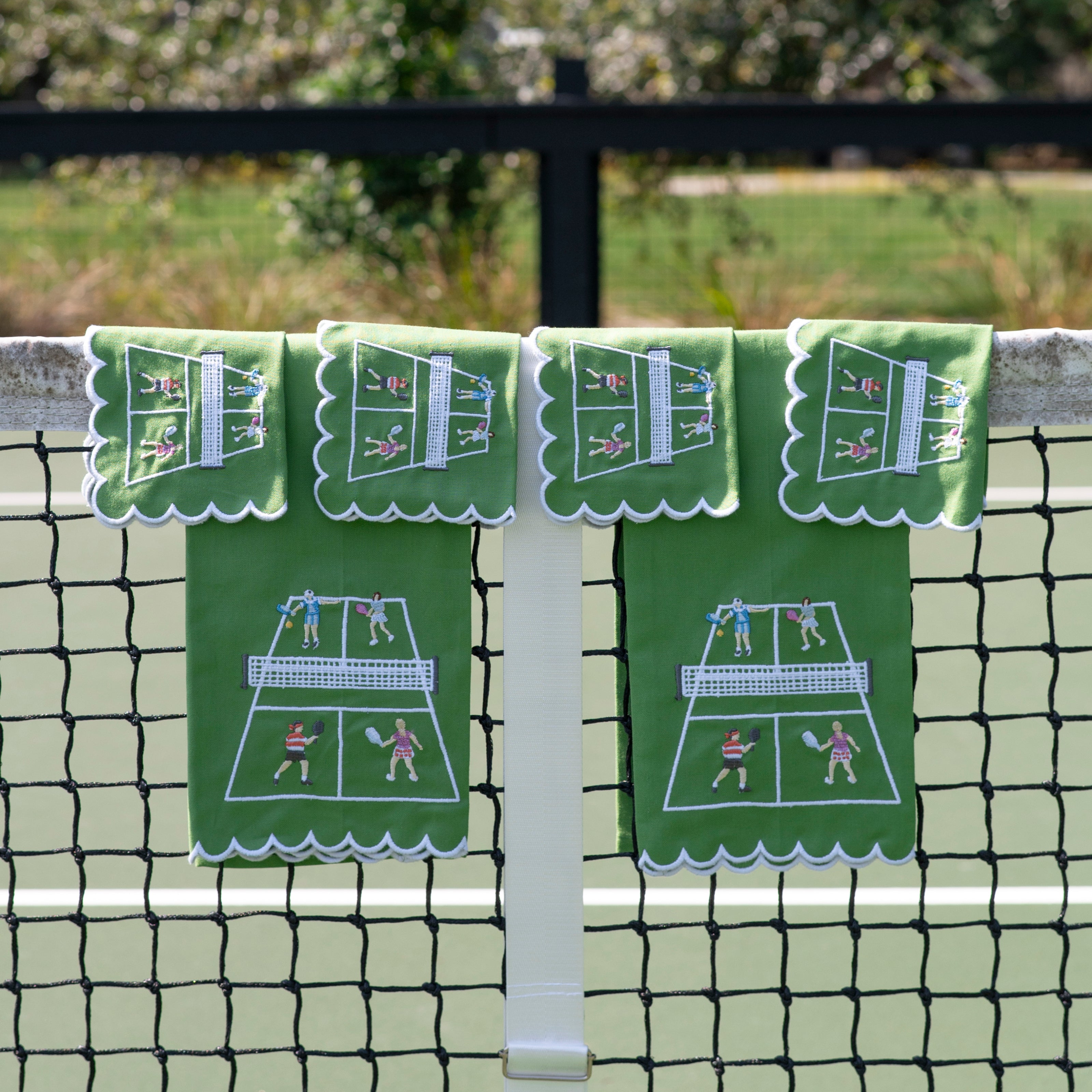 Green tea towels and cocktail napkins with pickleball design hanging on a net