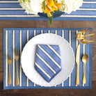 Table setting with blue and white striped placemat, white plate, gold cutlery, and floral centerpiece.