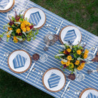 Outdoor table setting with blue and white striped tablecloth, floral arrangements, and decorative plates.