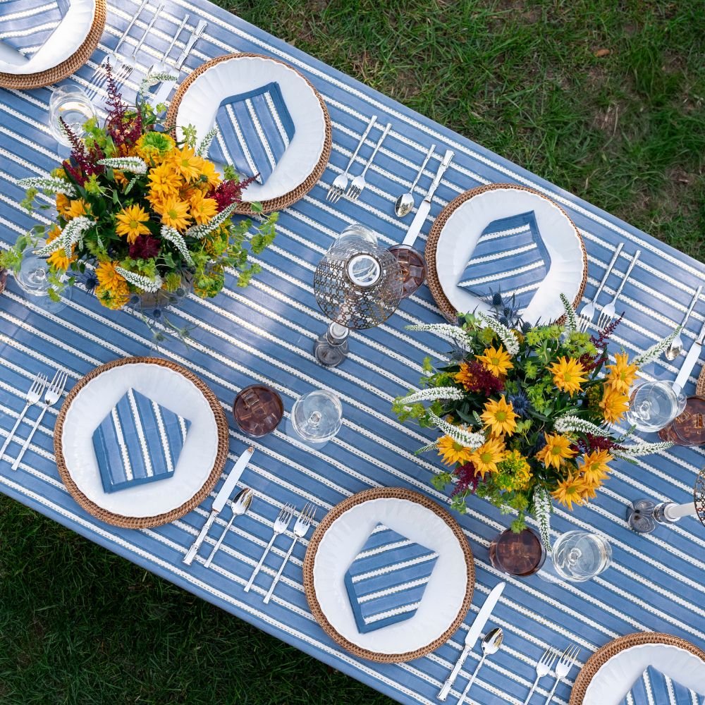 Outdoor table setting with blue and white striped tablecloth, floral arrangements, and decorative plates.