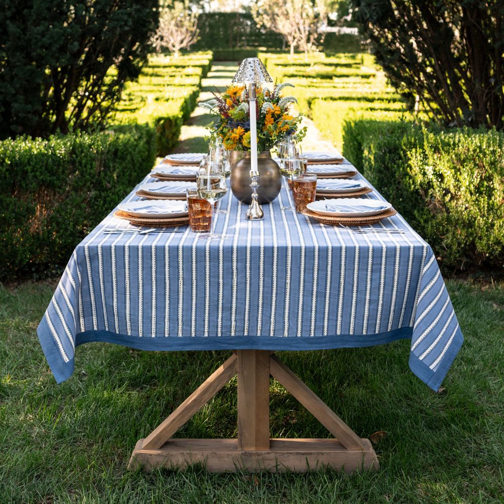 Dining table set with a blue and white striped tablecloth in an outdoor garden setting.