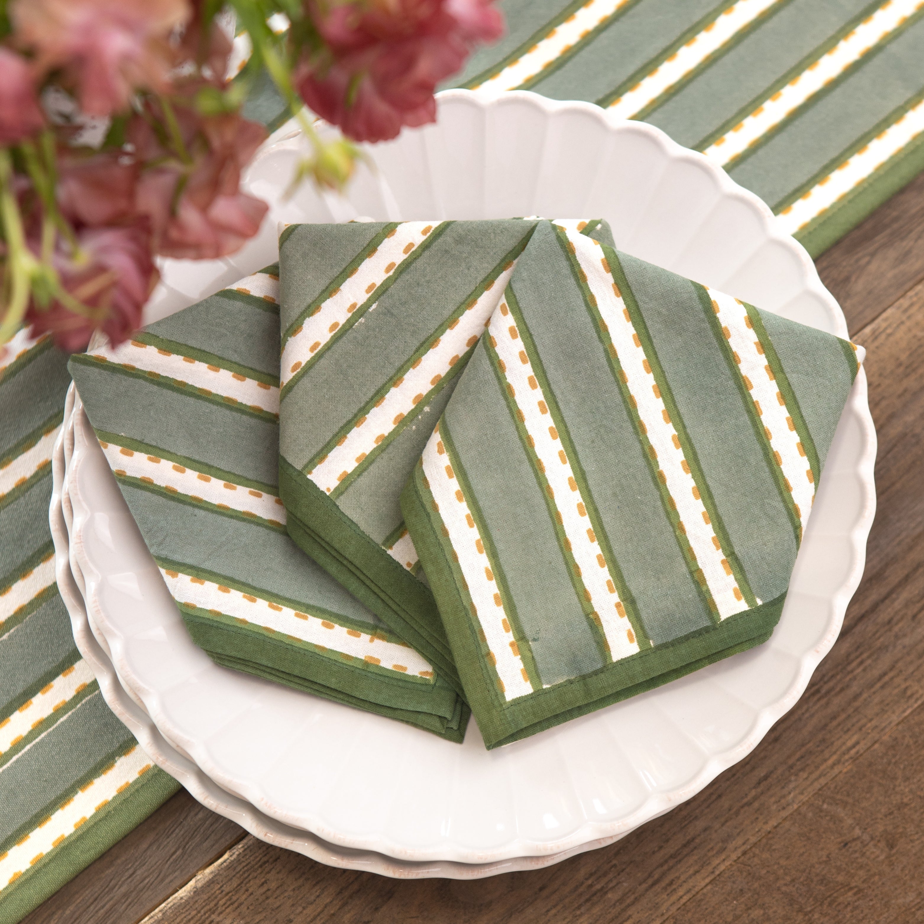 Green striped napkins on a white plate with flowers in the background