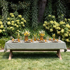 Dining table set for a meal outdoors with a striped tablecloth, sunflowers, and greenery.