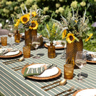 Outdoor table setting with sunflowers, glasses, and cutlery on a striped tablecloth.