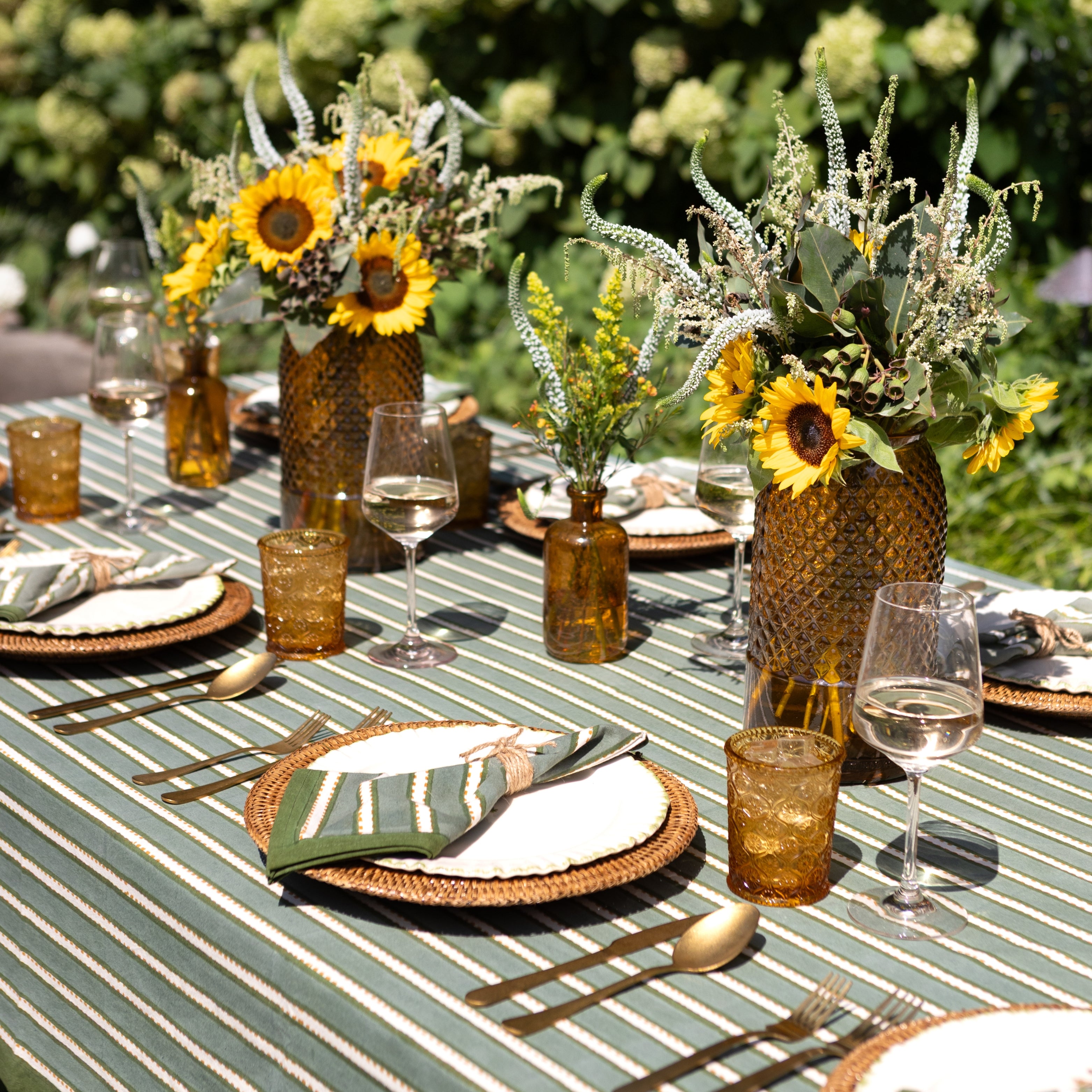 Outdoor table setting with sunflowers, glasses, and cutlery on a striped tablecloth.