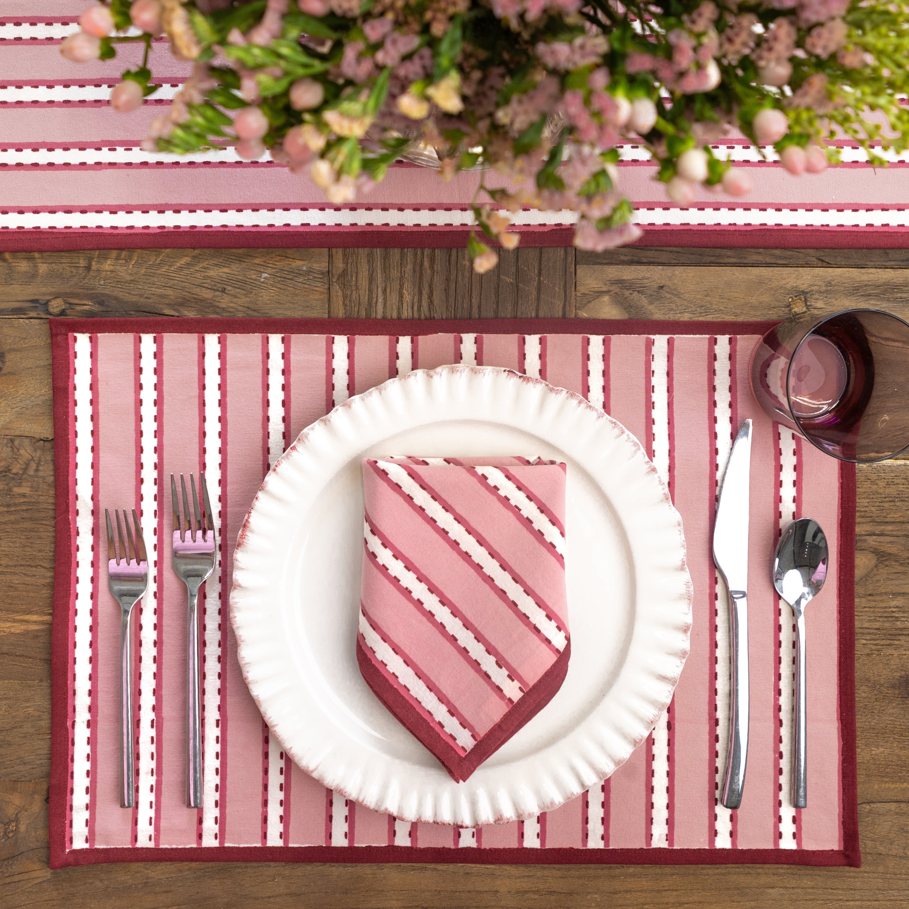 Dining table setting with rose and white striped placemat, plate, and napkin.