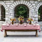Dining table set with a red tablecloth, floral centerpieces, and wine glasses in front of stone arches.
