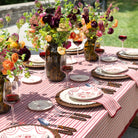 Elegant outdoor dining table setting with floral arrangements, red wine, and striped tablecloth.