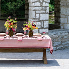 Dining table set with plates, glasses, and flowers outdoors near a stone building.