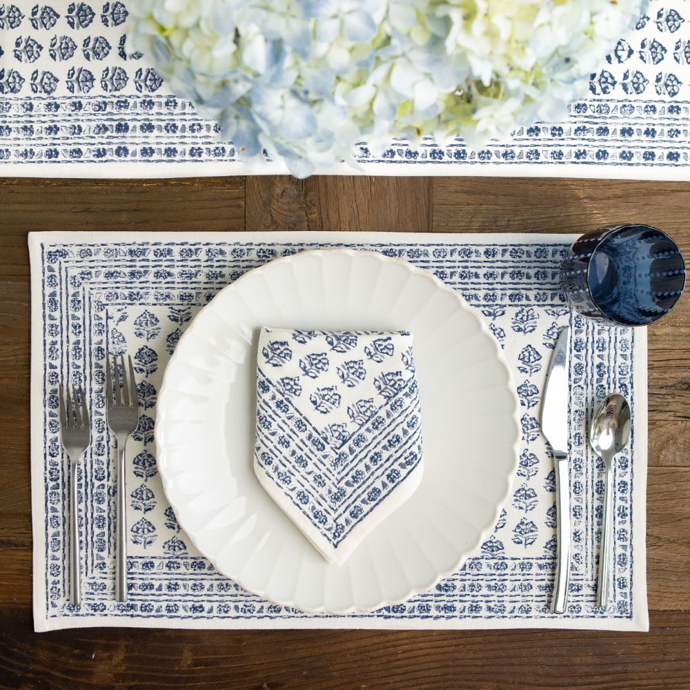 Table setting with blue and white patterned placemat, plate, and napkin on a wooden table.