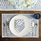 Table setting with blue and white patterned placemat, plate, and napkin on a wooden table.