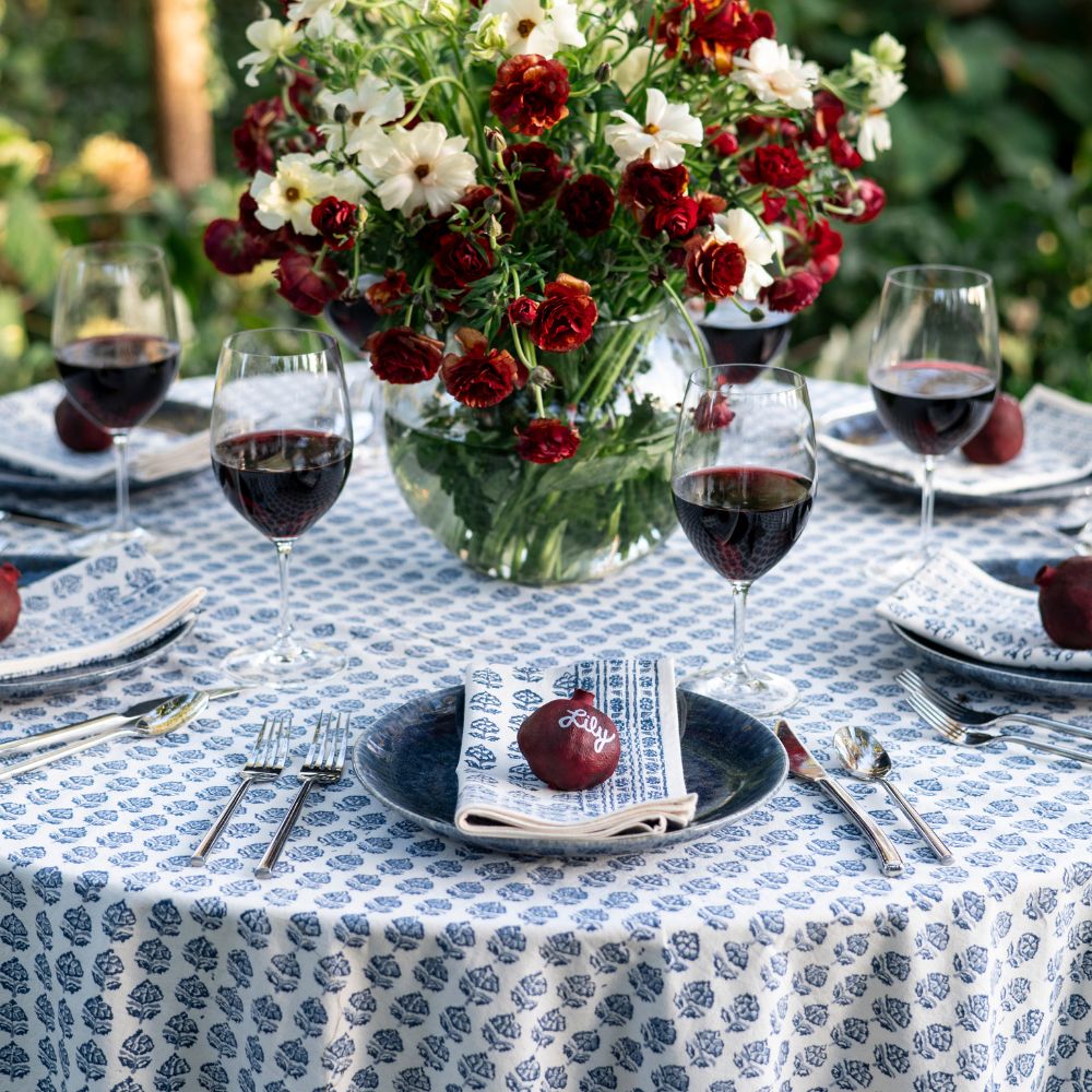 Table setting with red wine, flowers, and a floral tablecloth.
