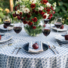 Table setting with red wine, flowers, and a floral tablecloth.