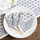 Set of blue and white patterned napkins on a white plate with a floral tablecloth in the background.