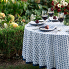 Table set with wine glasses, plates, and flowers outdoors on a patterned tablecloth.