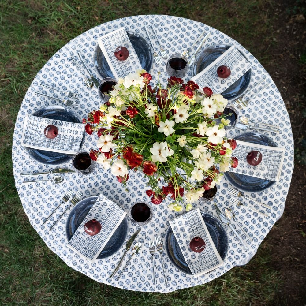 Round table set with blue and white patterned tablecloth, floral centerpiece, and pomegranates.