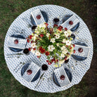 Round table set with blue and white patterned tablecloth, floral centerpiece, and pomegranates.