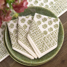Set of patterned napkins on a green plate with flowers in the background