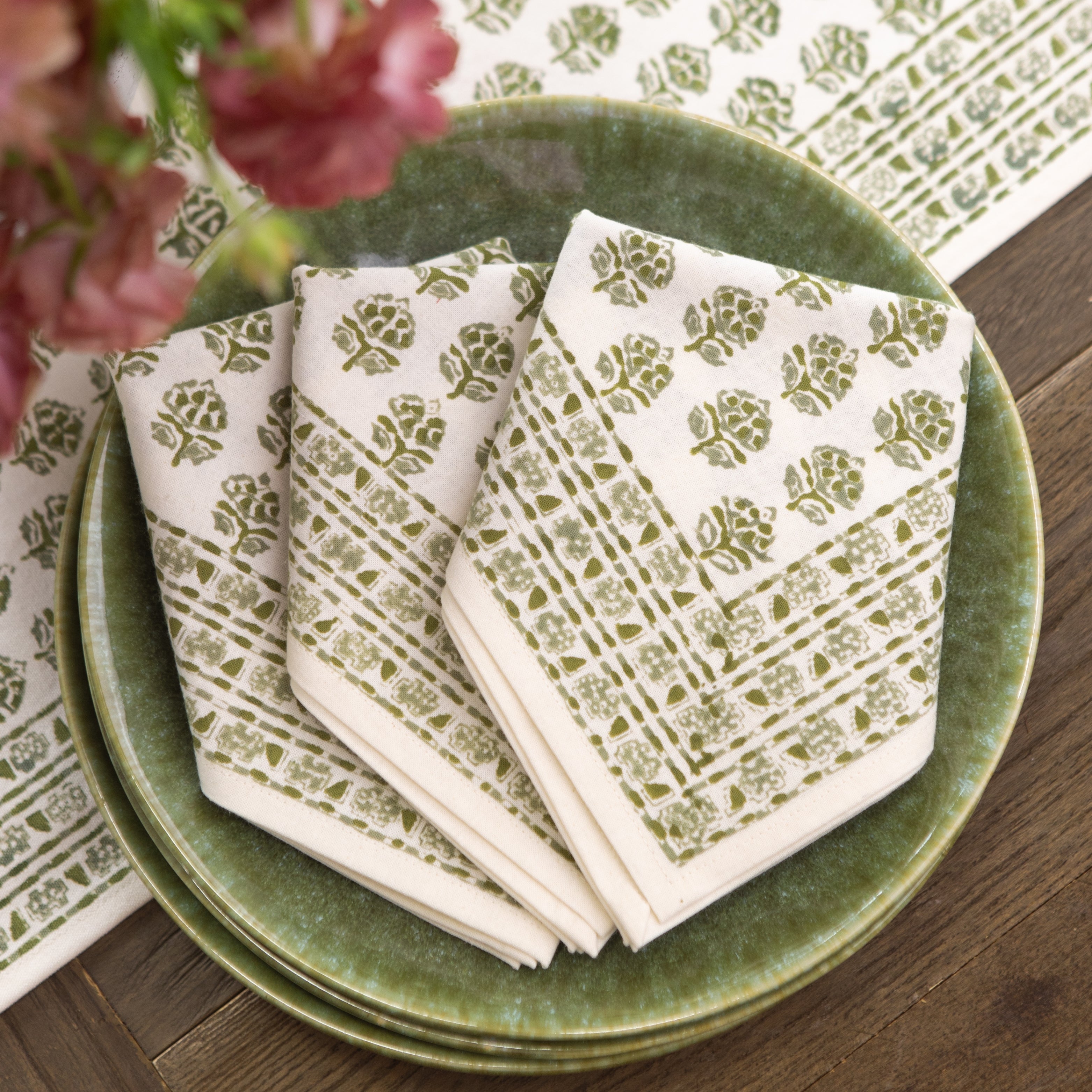 Set of patterned napkins on a green plate with flowers in the background