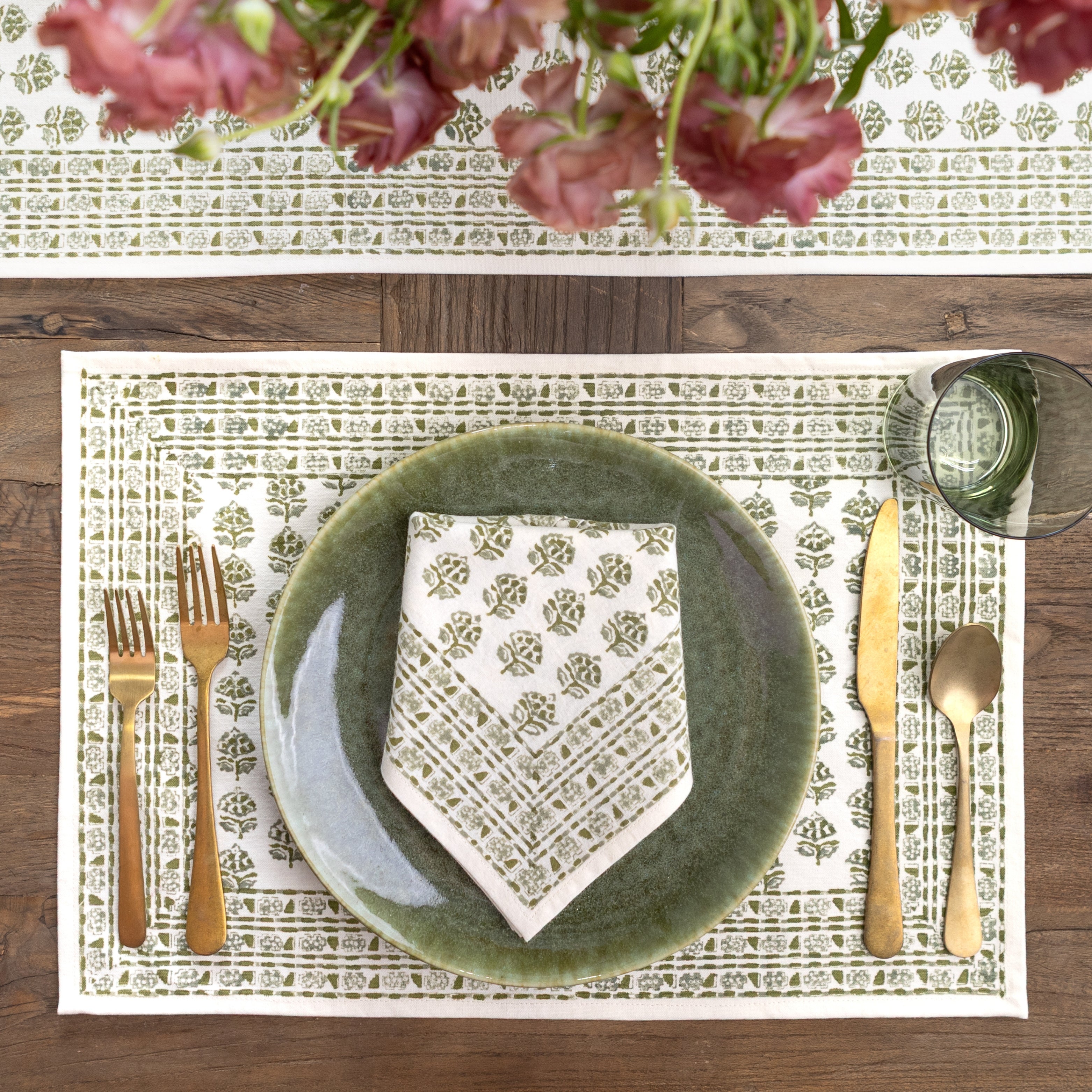 Table setting with green plates, gold cutlery, and a floral centerpiece.
