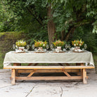 Dining table set outdoors with floral centerpieces and a green printed tablecloth.