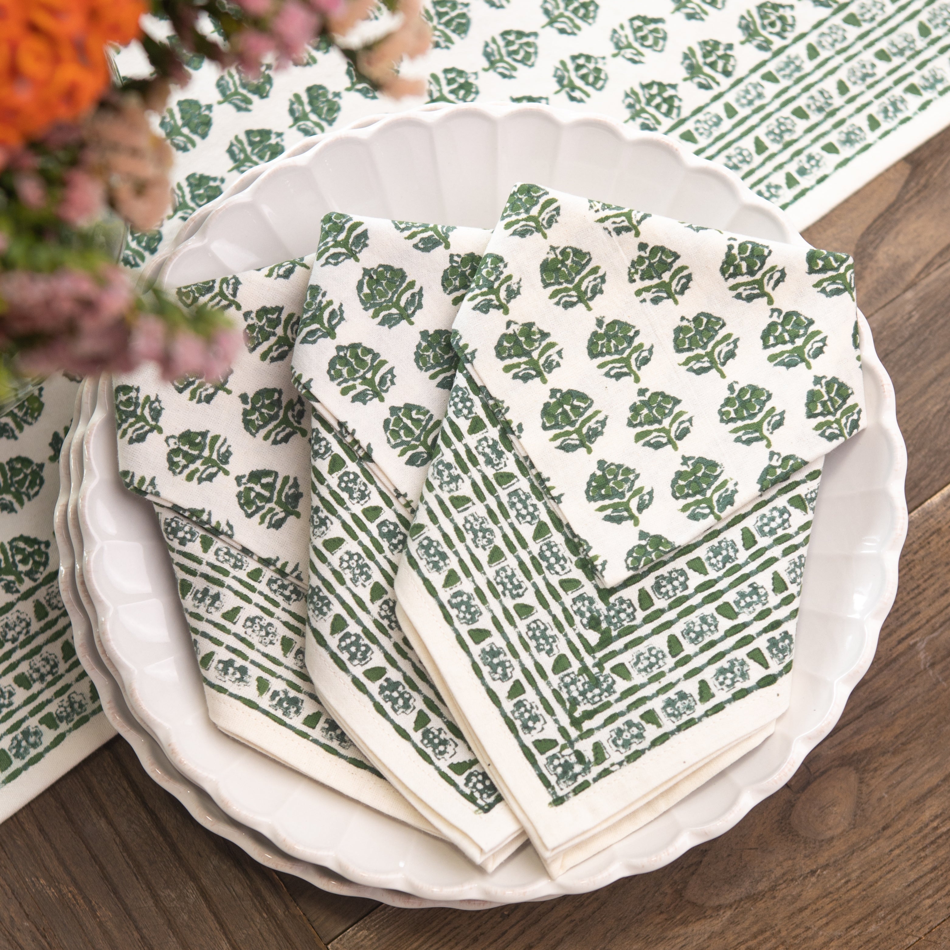Set of green and white patterned napkins on a wooden table with flowers.