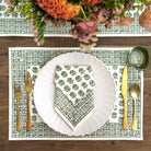 Table setting with a green patterned placemat, white plate, and gold cutlery on a wooden table.