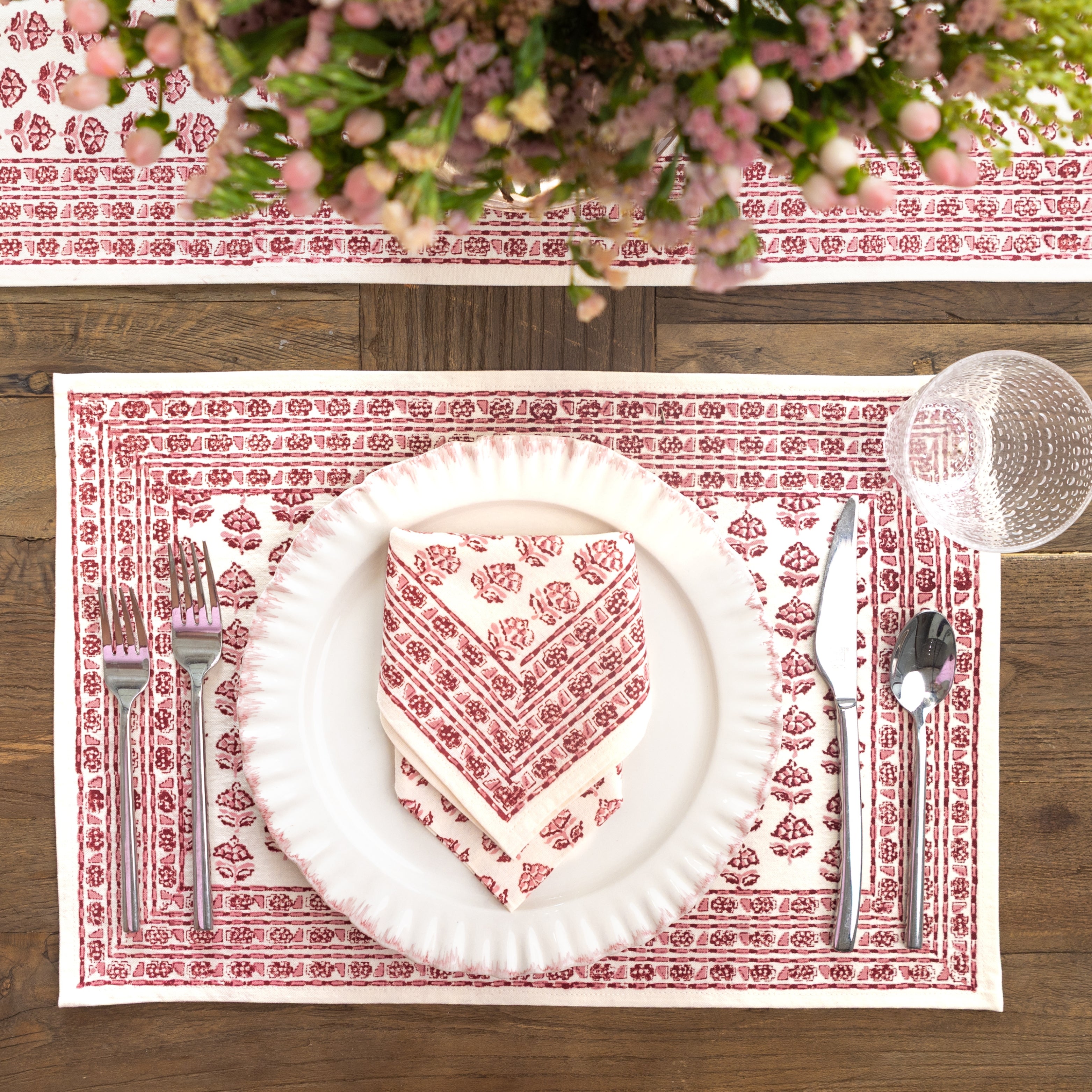 Table setting with white plate, cutlery, and floral arrangement on a patterned placemat.