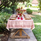 Dining table set outdoors with a floral arrangement and red vases on a red patterned tablecloth.