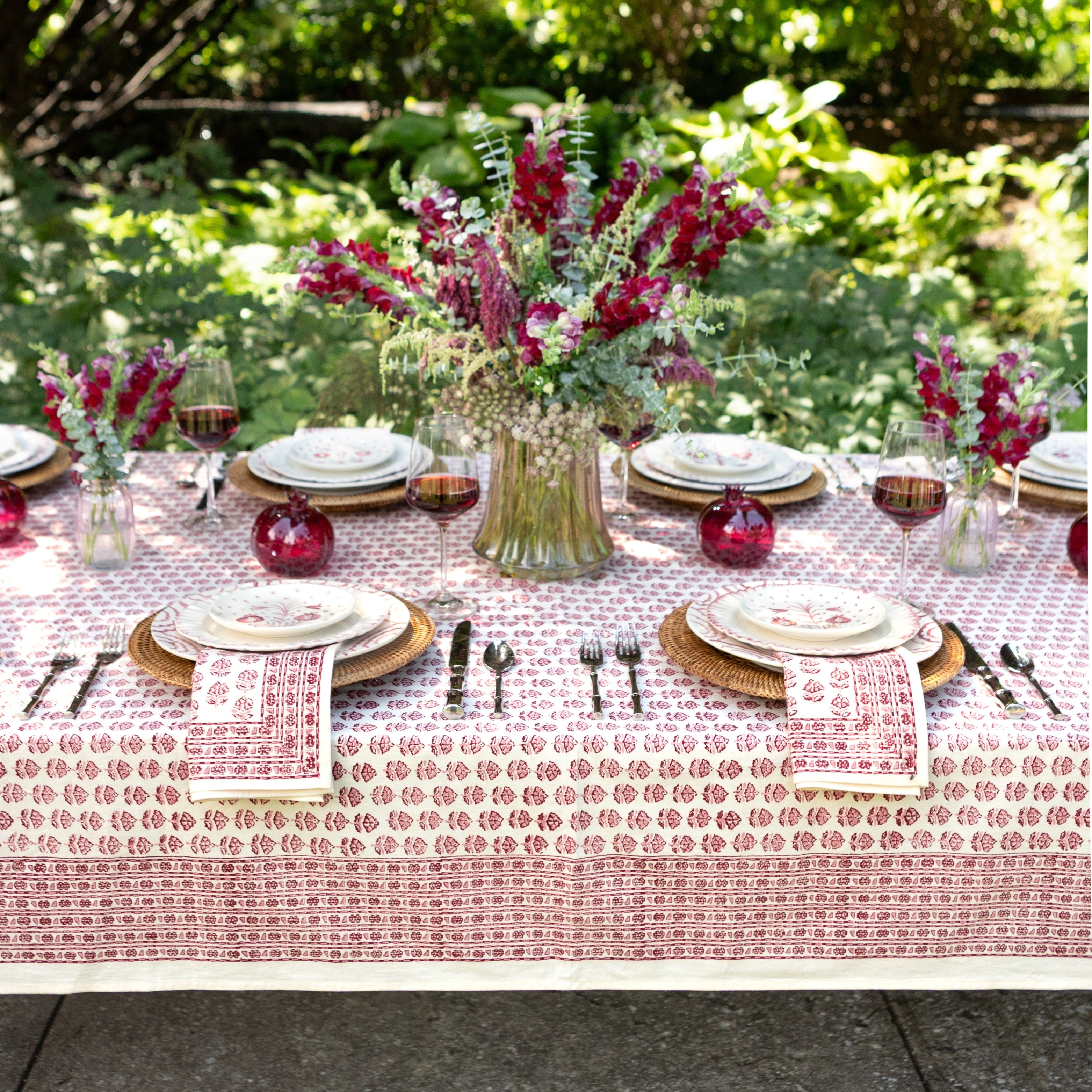 Elegant outdoor table setting with floral centerpieces and red patterned tablecloth.