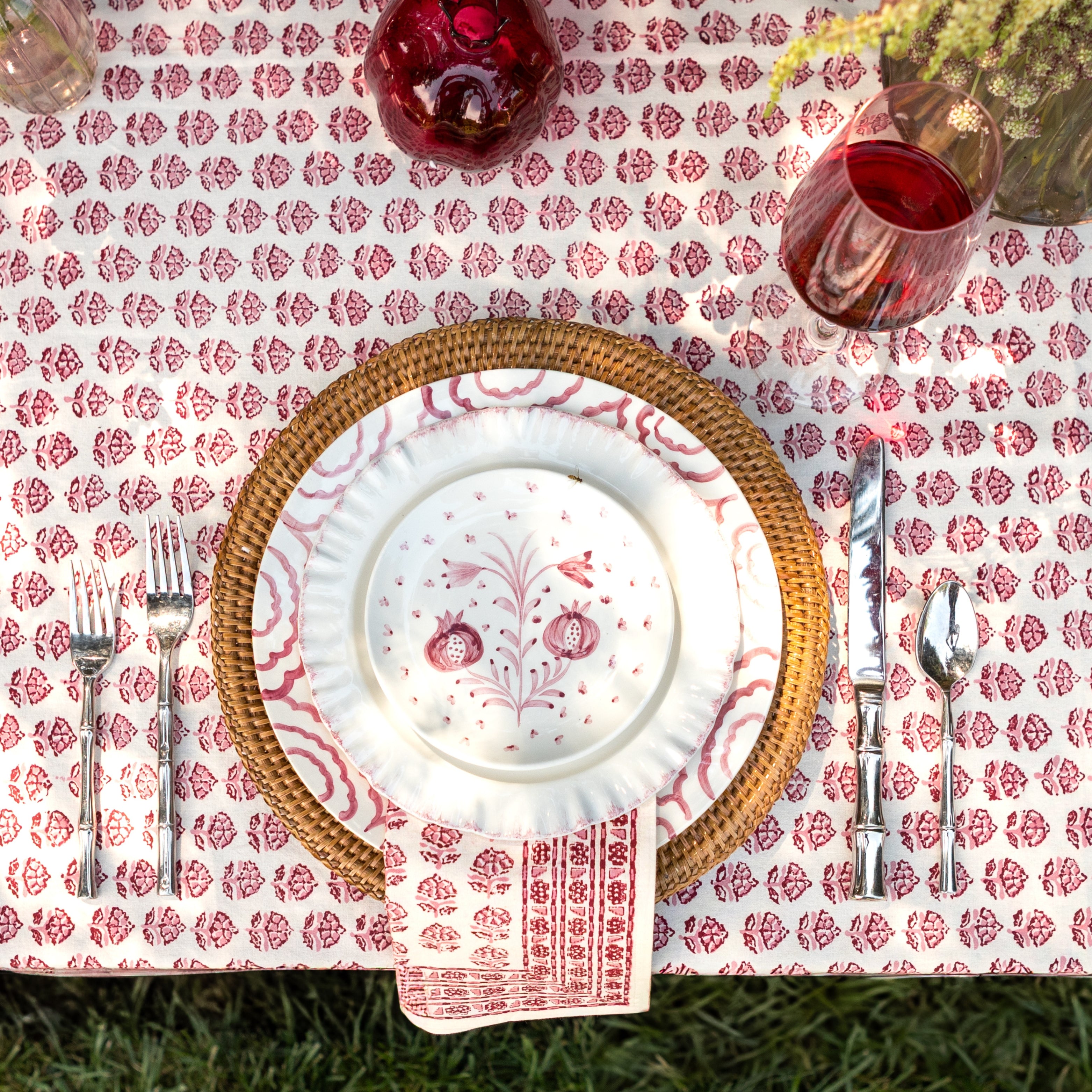 Table setting with floral tablecloth, plates, cutlery, and glasses.