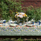 A colorful floral tablecloth with yellow, blue, and red flowers displayed on a table outdoors.