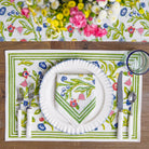 A set of four placemats with a floral pattern in shades of yellow, blue, and red, displayed on a table with a plate and cutlery.