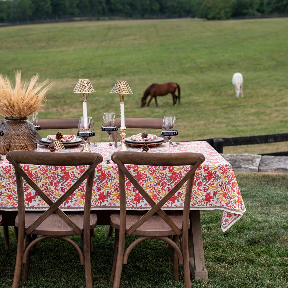Dining table set with a floral tablecloth in an outdoor setting with horses in the background.