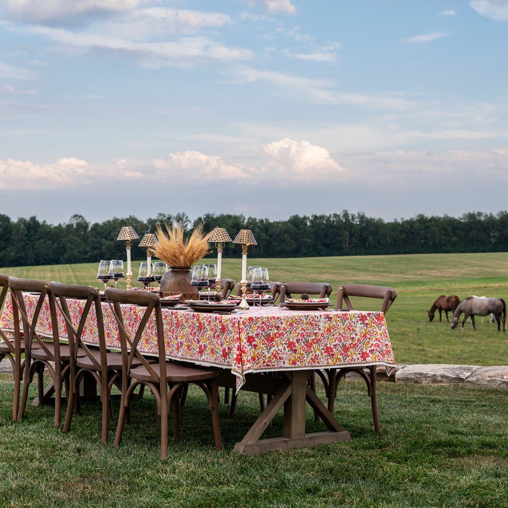 Dining table set outdoors with floral tablecloth and chairs, horses grazing in the background.