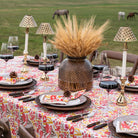 Dining table set with floral tablecloth, decorative vase, and outdoor background with animals.