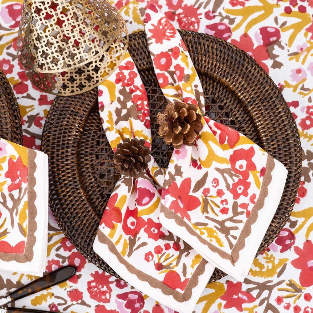 Floral-patterned napkins on a decorative table setting with woven placemats and pinecones.