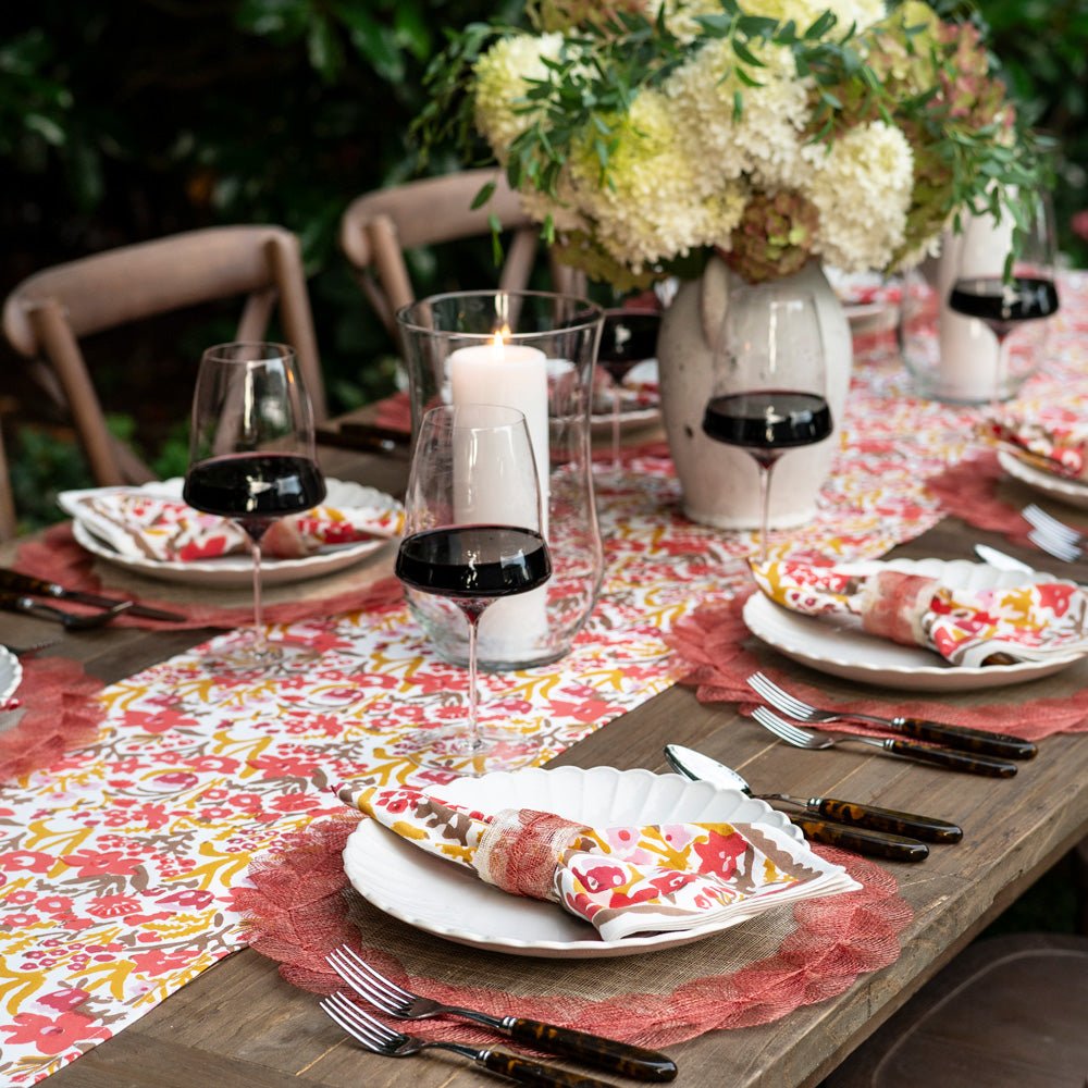 Dining table set for a meal with floral tablecloth, wine glasses, and cutlery.
