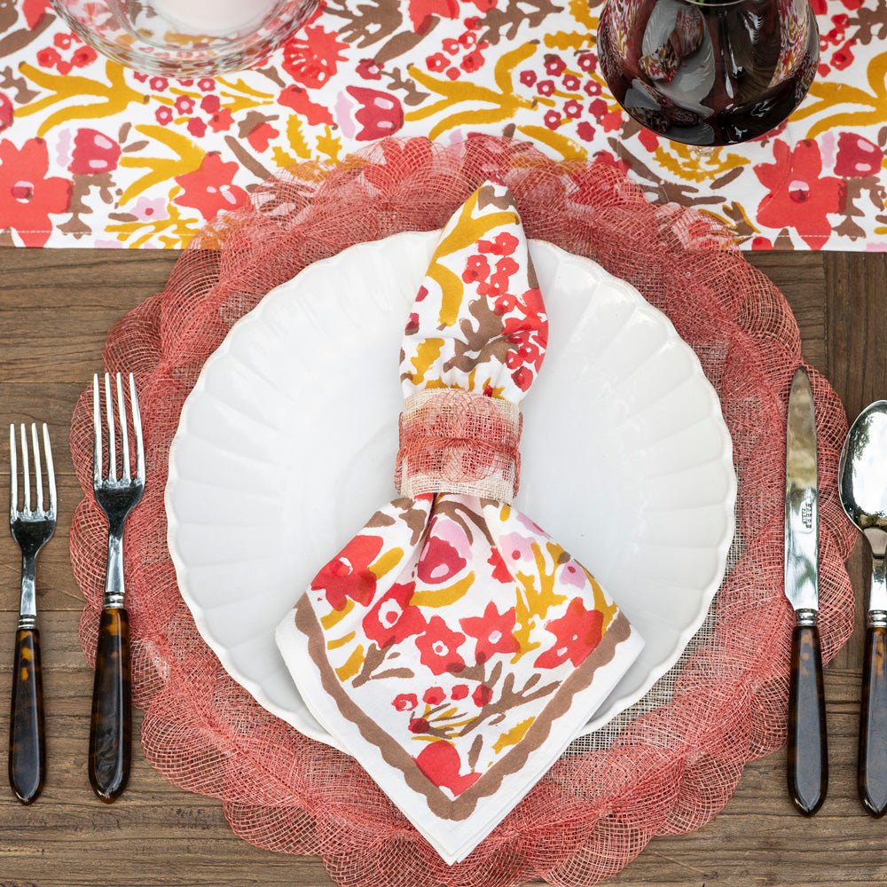 Dining table setting with floral napkin, white plate, and cutlery on a colorful tablecloth.